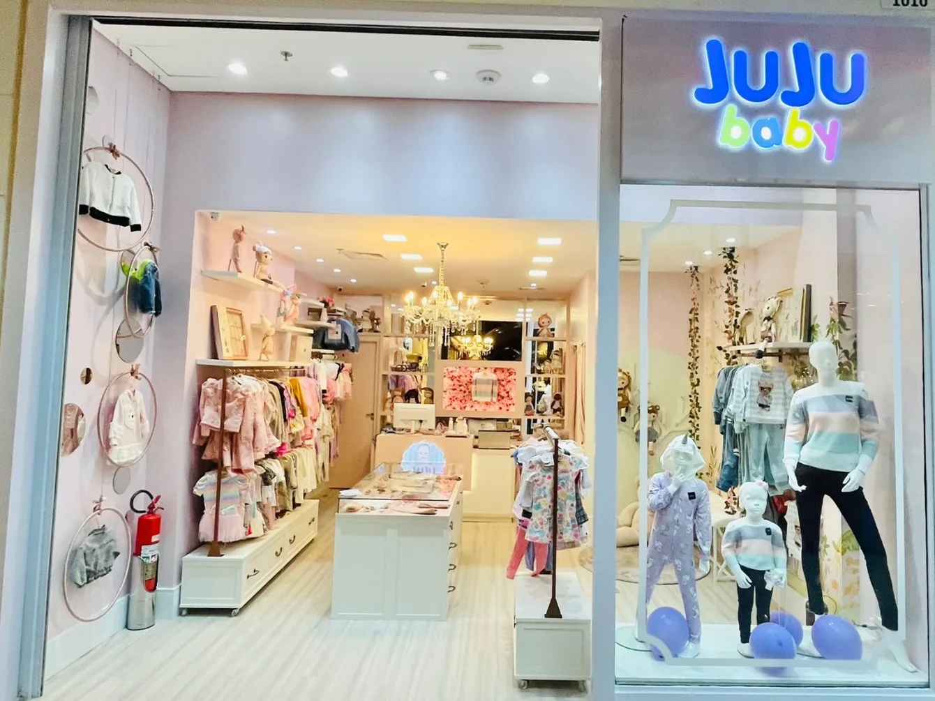 Fachada executada da loja Juju Baby, com vitrine emoldurada e arcos com roupas suspensas